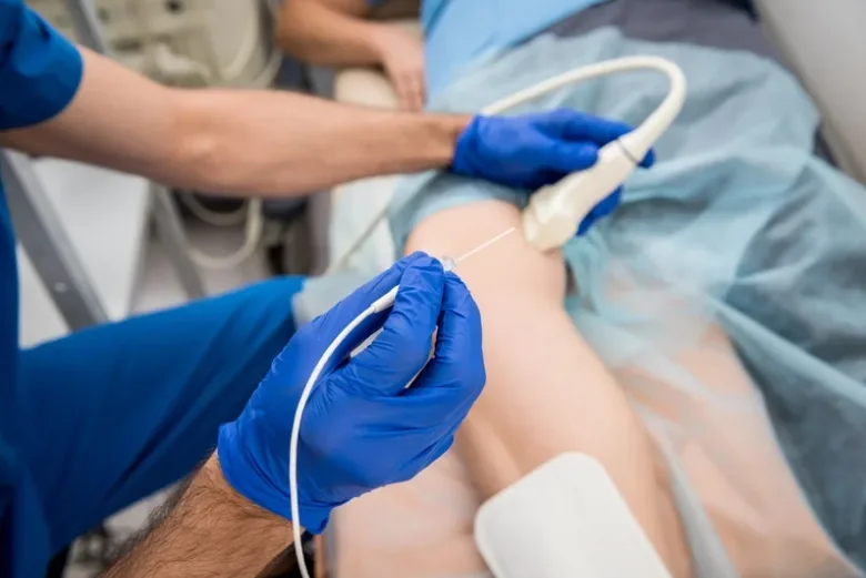 Specialist holding an ultrasound probe during a leg radiofrequency ablation procedure.